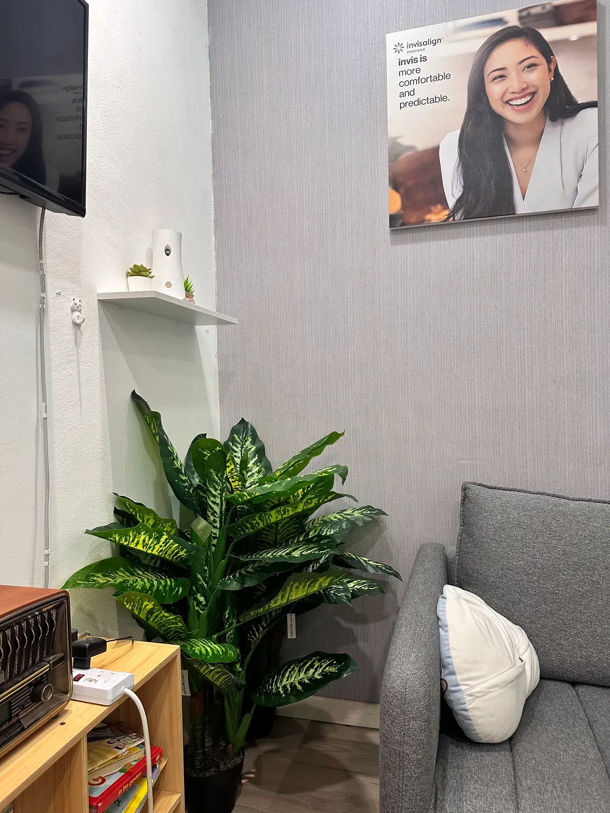 Quiet waiting corner with a grey sofa, cushions and a leafy plant at our Bukit Jalil dental clinic