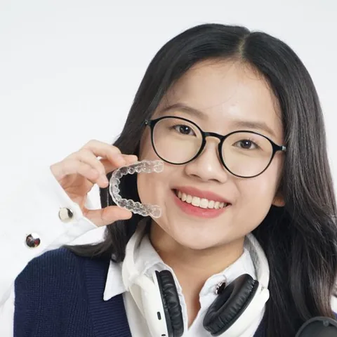 Smiling young woman holding up her clear Invisalign aligner