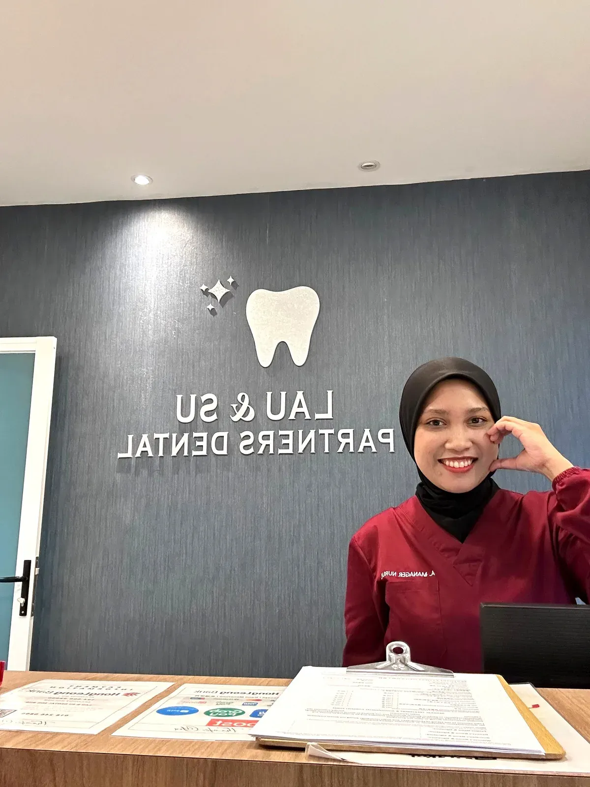 Receptionist at the front desk beneath the Lau & Su Partners Dental sign, ready to check patients in at the Bukit Jalil clinic